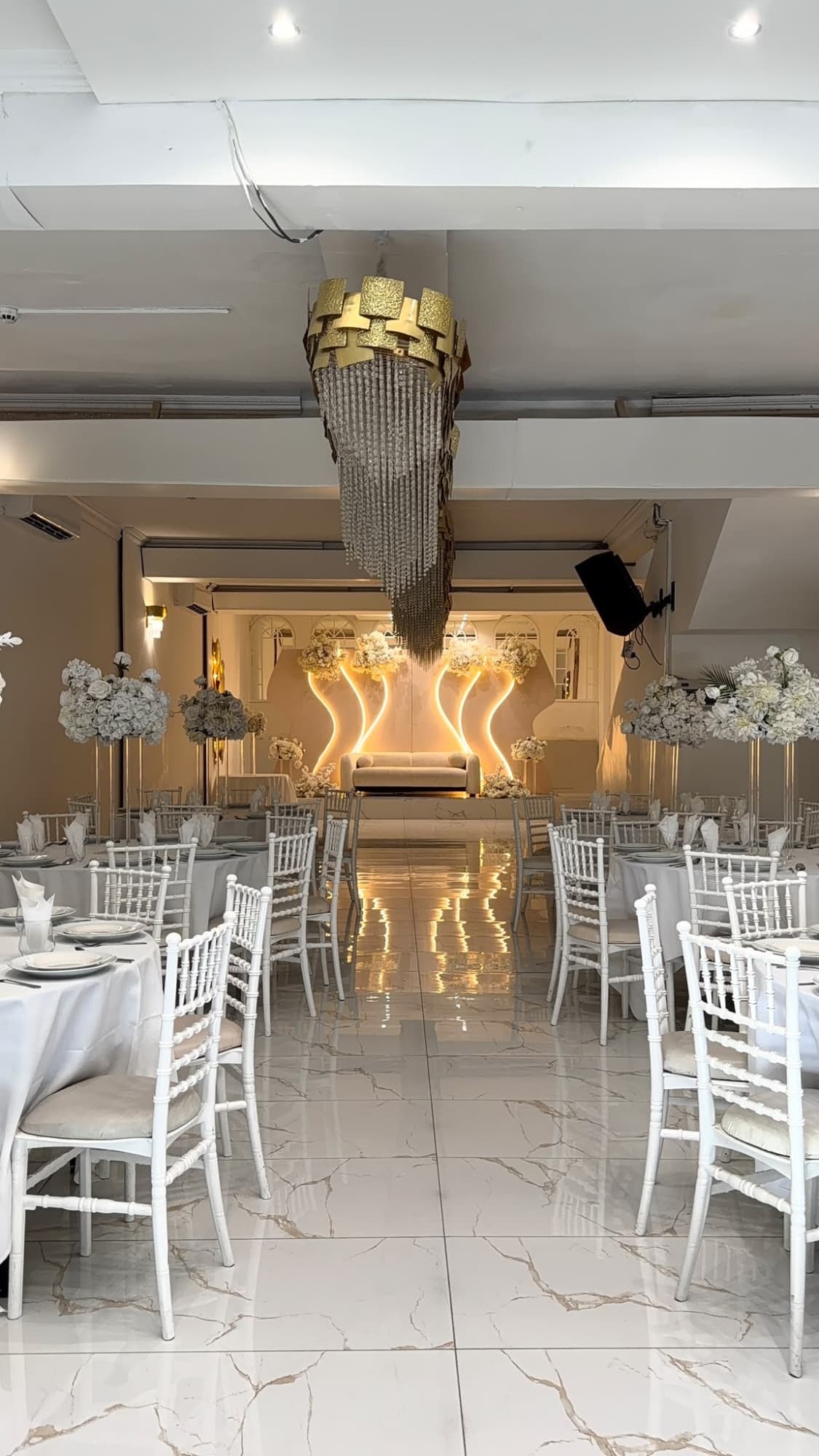 The hall dressed for a reception, with a marble aisle, white chairs, and a lit stage