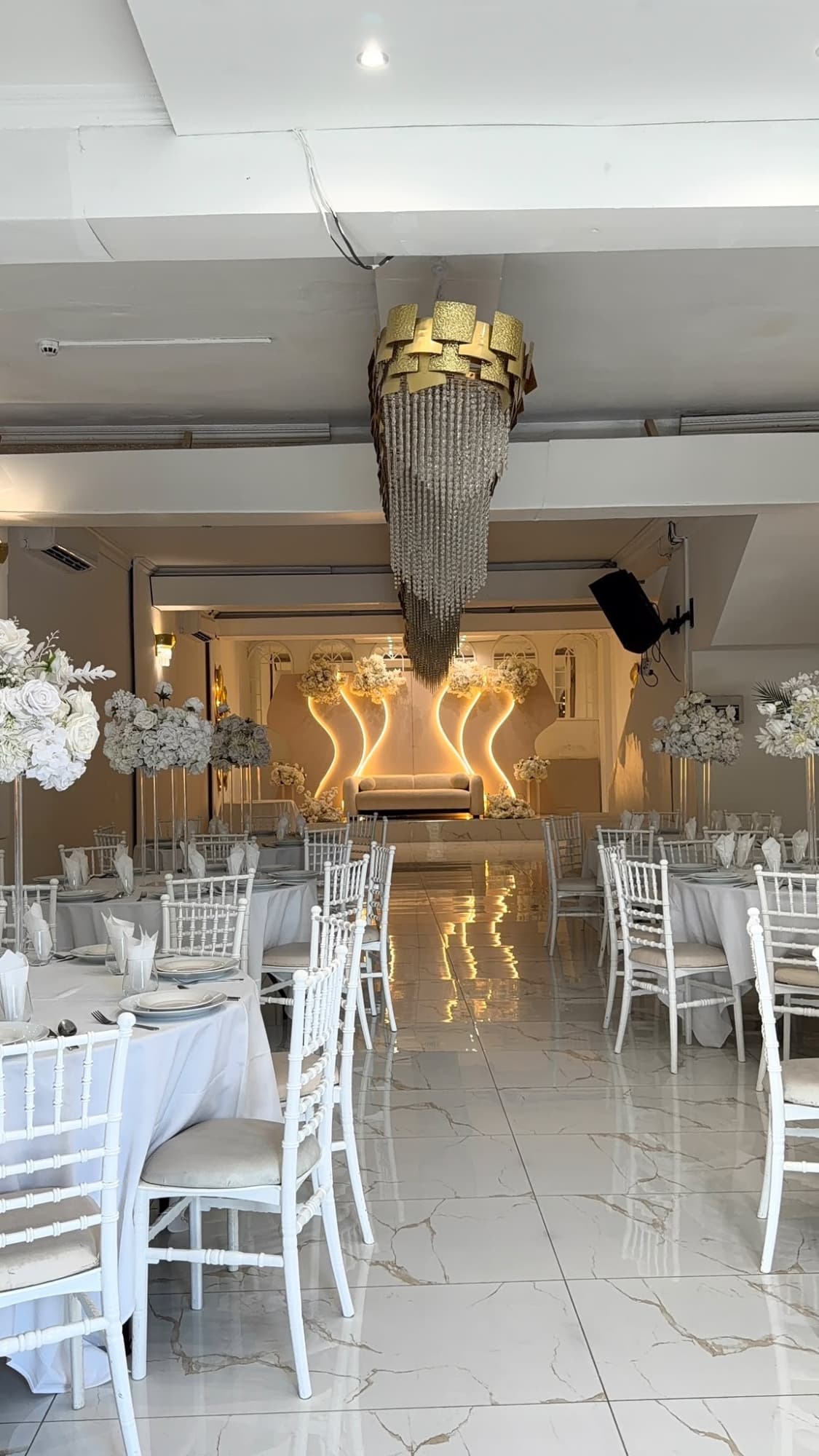 A long view of the hall toward the stage, with round tables and white chairs on both sides