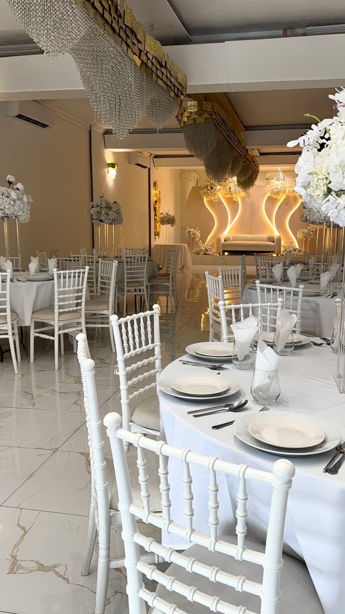 The hall set for a party, with round tables, white chairs, and the stage beyond