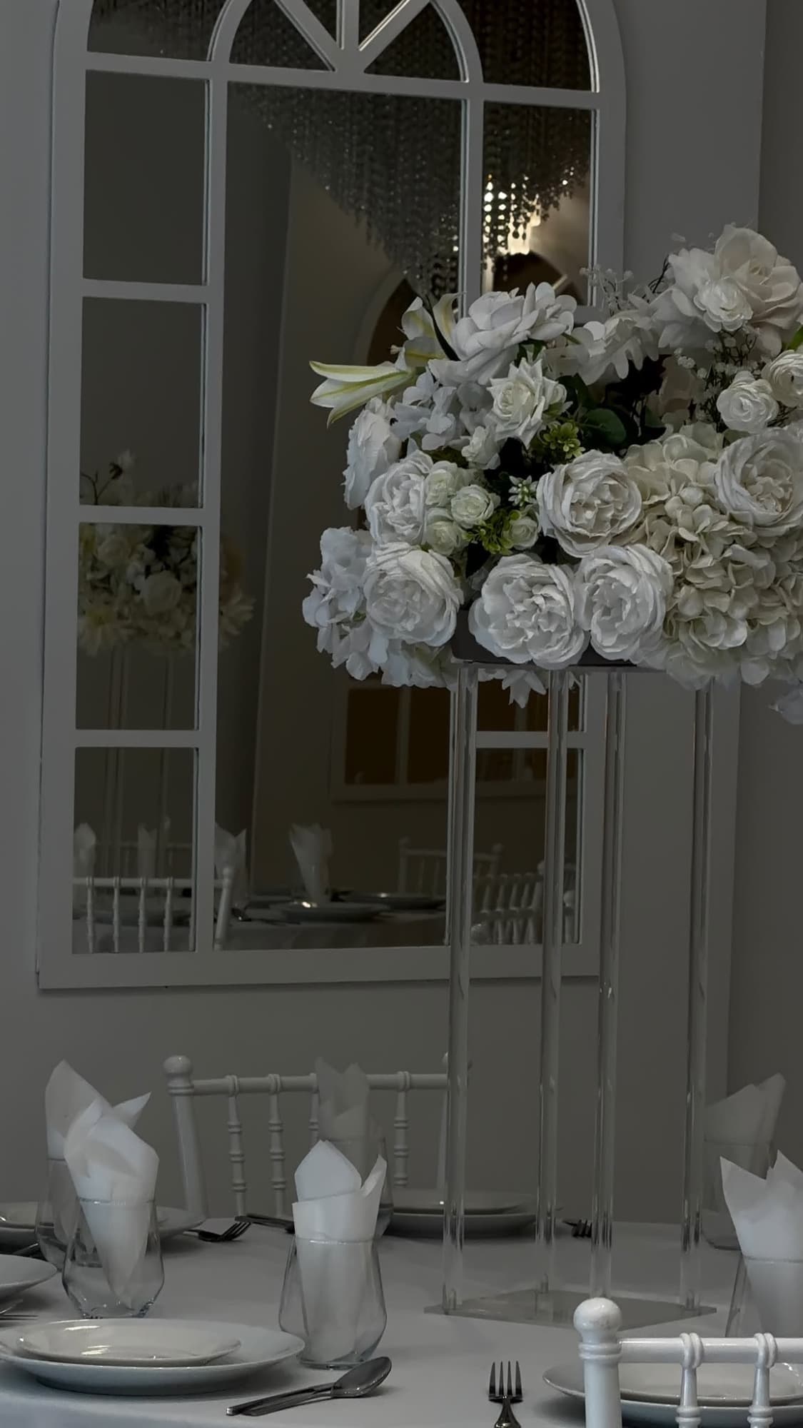 White flowers beside a laid table and an arched mirror