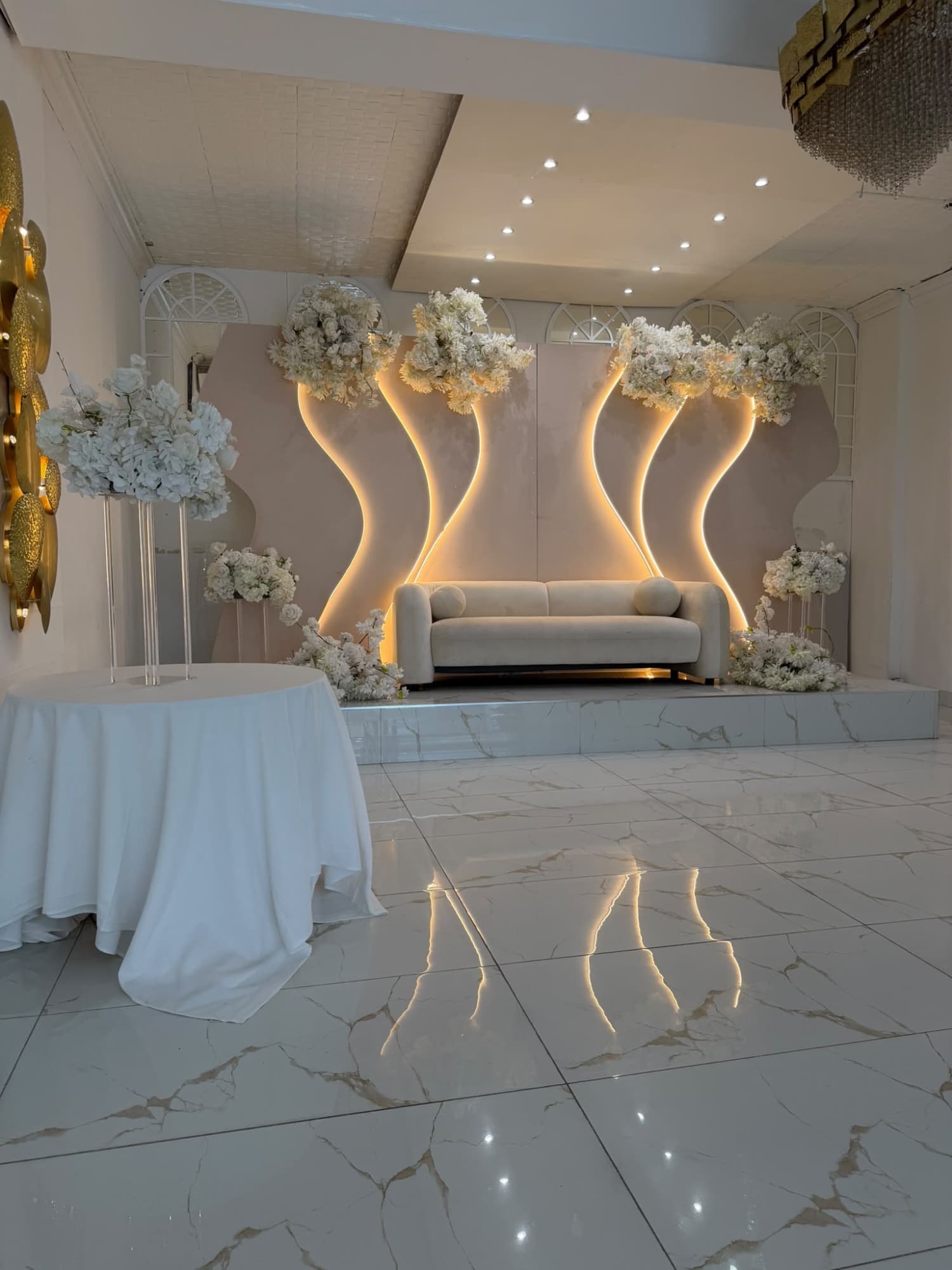 A cream sofa on the marble stage, framed by gold light and white flowers