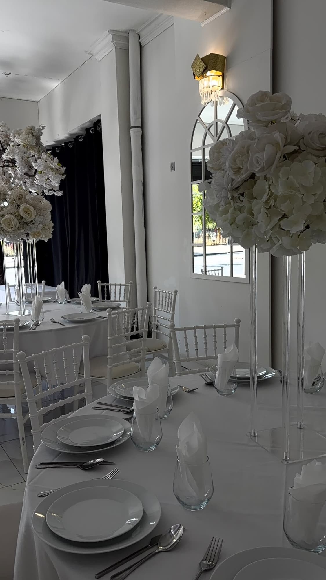 A round table set in white, beside an arched mirror and a wall light